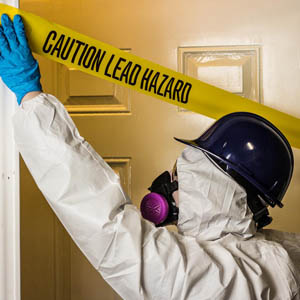 employee in a hazmat suit and ventalator putting up hazard tape over a doorway