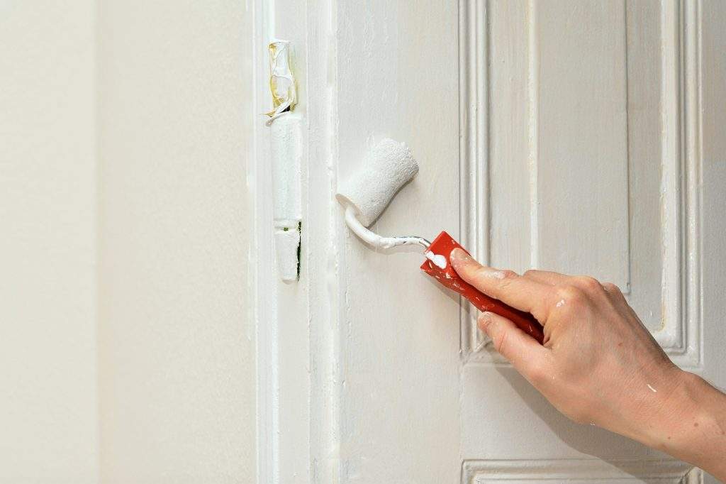 person using a short paint roller to apply white paint to a door, understanding lead paint testing